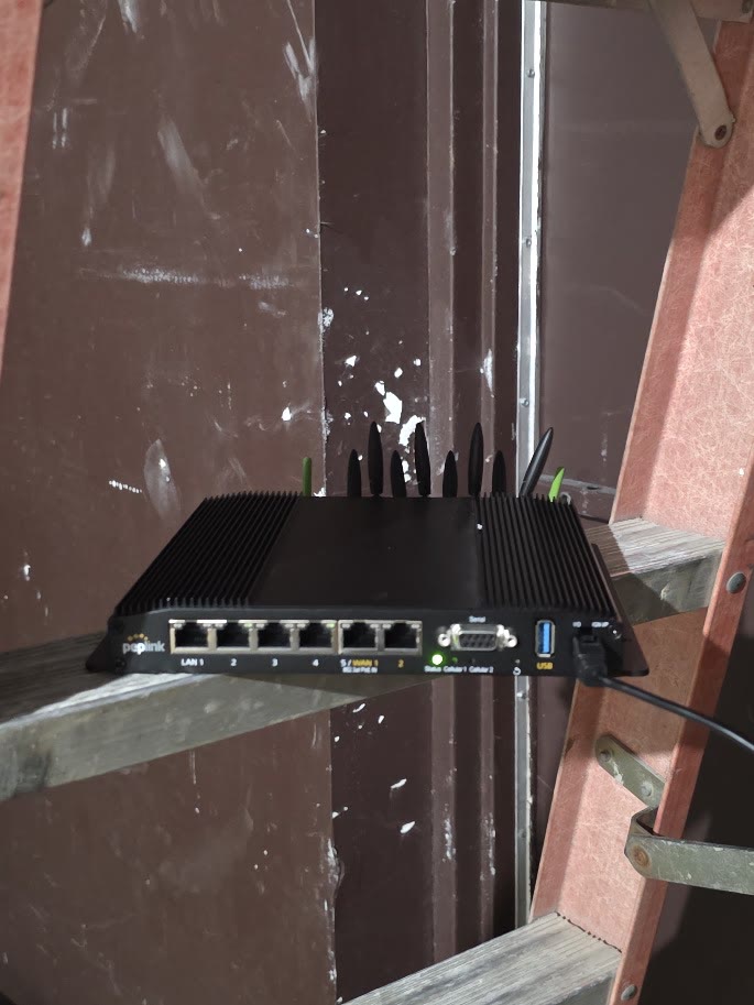 A Peplink MAX BR2 Pro 5G sitting on a ladder shelf in an unfinished retail space, antennas up.