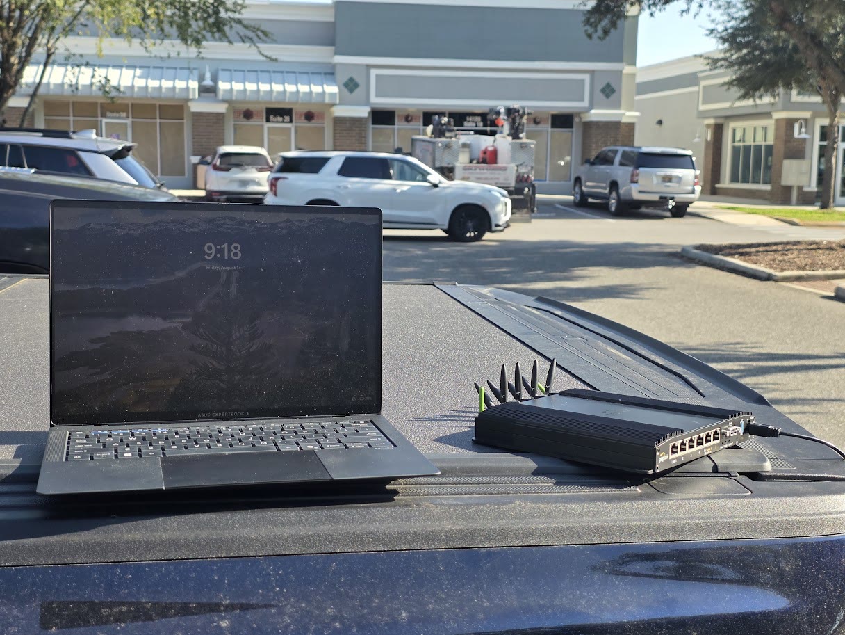 A laptop and a Peplink BR2 Pro 5G on a truck tailgate in front of an empty storefront during a site survey.